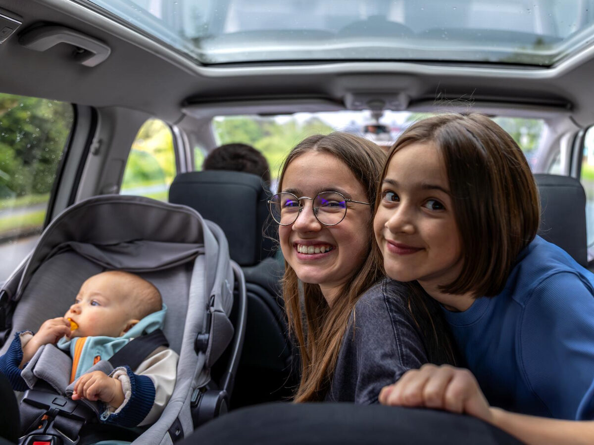 A parent securing a child into a child seat in the back of a taxi